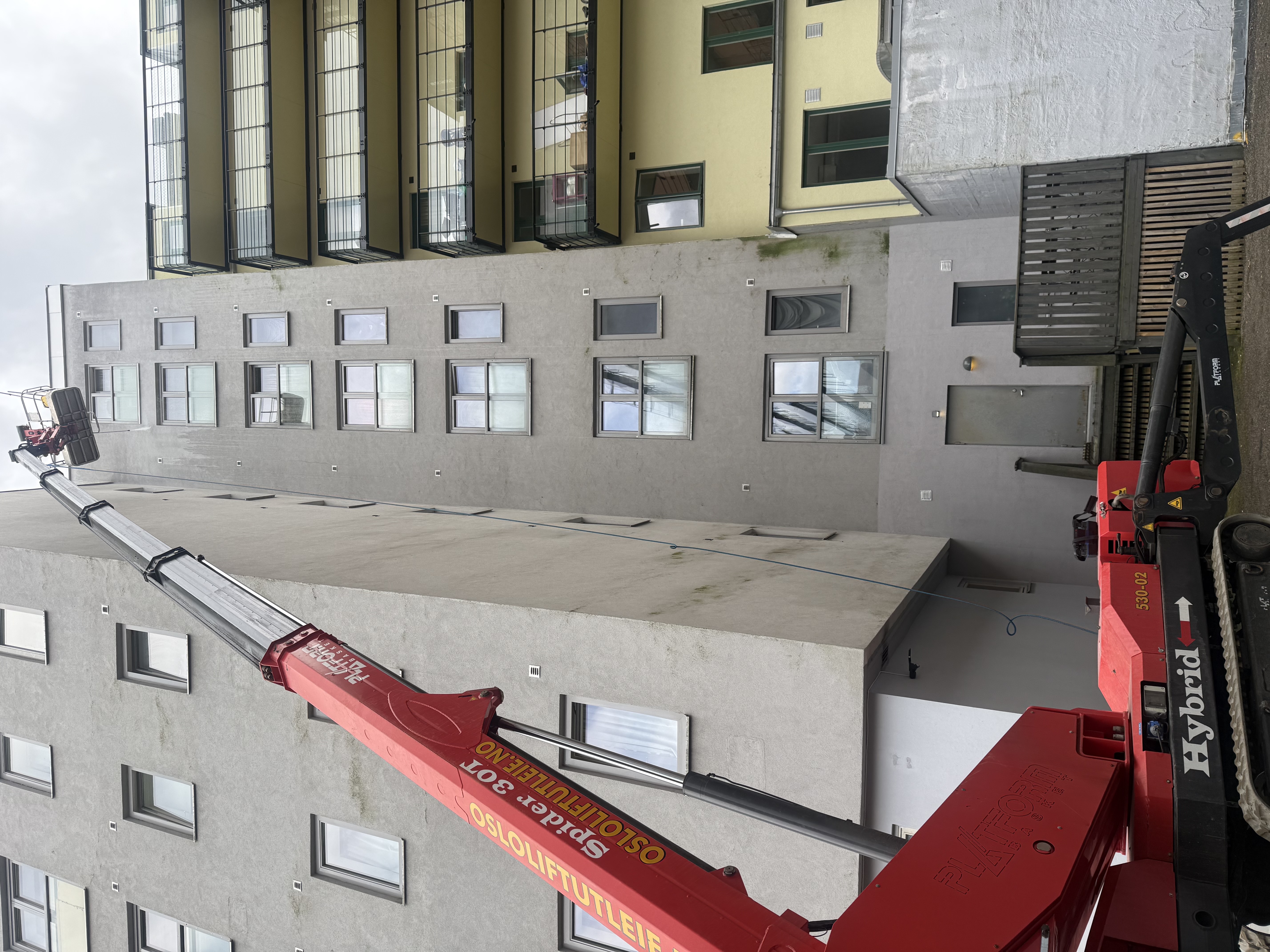 Profilert servicebil med lift parkert foran høyblokk hos næringseiendom